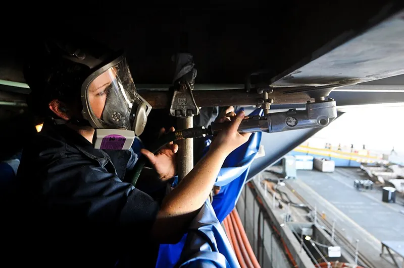 Sailor removing failed paint from steel before recoating to avoid marine coating failures