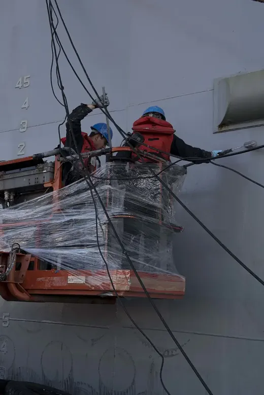 Painter applying coating to a ship hull, following TDS paint application limits